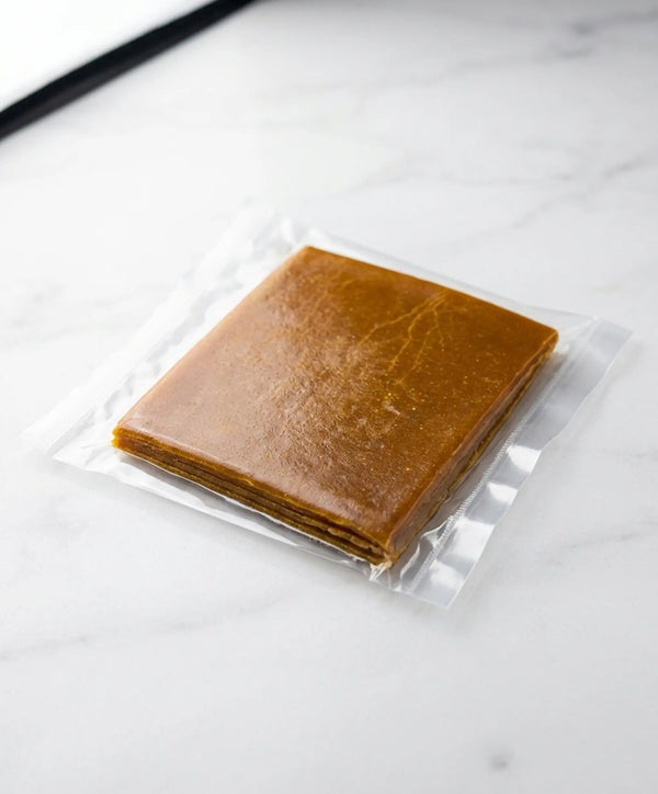 Close-up shot of an authentic square block of Sindhuswad Amba Poli in clear plastic packaging, showcasing the rich golden-orange color and distinct chewy layers of natural mango fruit leather.