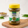 A jar of Sindhuswad Foods Mirchi Lonche (chili pickle) on a wooden cutting board, with green chilies and a small bowl of spices in the background.