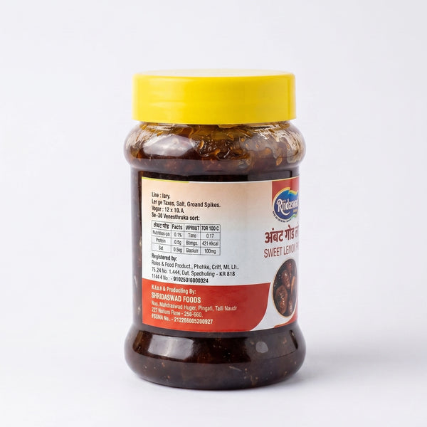 A jar of  Sindhuswad Foods Sweet Lemon Spice paste on a clean white background. The product is in a clear plastic jar showing the dark brown paste inside, topped with a bright yellow cap, and has a white and red label.